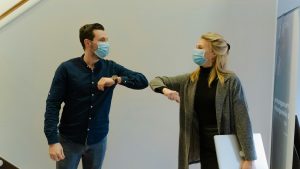 Two office workers in London wearing face masks and greeting with elbow bump as part of COVID-19 secure daily office cleaning protocol.